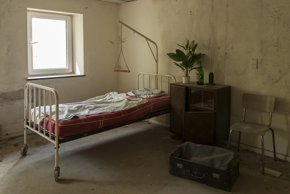 leegstaande kamer met bed en reiskoffer in het verlaten en
            vervallen De Gensterbloem, het verzorgingstehuis bij de bekende
            urbex locatie Agnus Dei